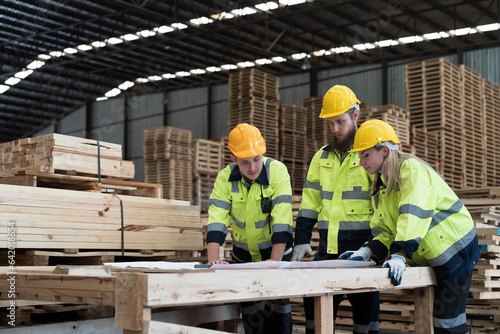 Male and female warehouse workers working and inspecting quality of plank of wood on shelves pallet at wooden warehouse storage. Group of warehouse workers discussing, checking products in warehouse