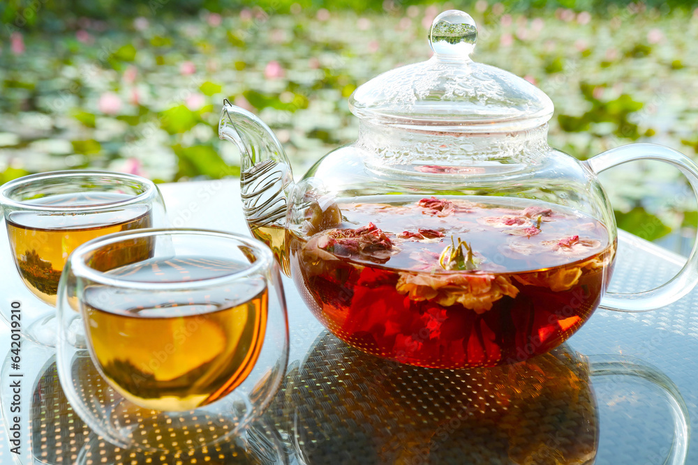 Closeup of a pot of rose tea with two cups of tea on garden table Closeup of a pot of rose tea with two cups of tea on garden table