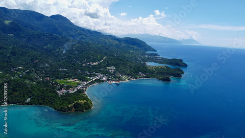 The coast of a tropical island in the Pacific Ocean. Cape of the island, hills, bay, lagoon, strait, small settlement on the seashore. © Houston