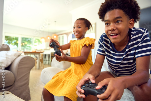 Brother And Sister Sitting On Sofa At Home Playing Video Game Together