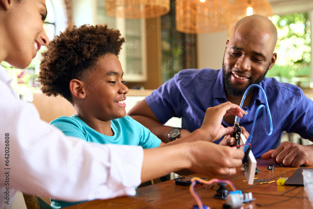 Family Around Table At Home Using Laptop With Parents Helping Son With Science Homework Family Around Table At Home Using Laptop With Parents Helping Son With Science Homework
