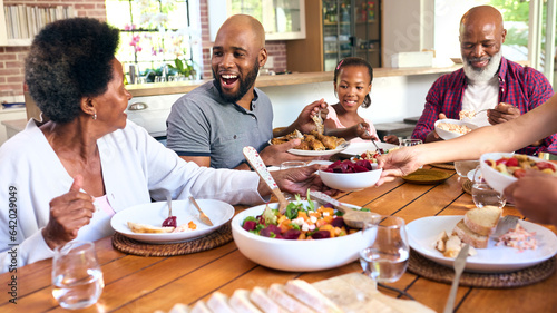 Multi-Generation Family Sitting Around Table Serving Food For Meal At Home Together