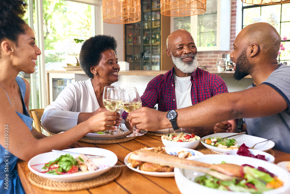 Senior Parents With Adult Offspring Sitting Around Table Doing Cheers With Wine Before Meal At Home Senior Parents With Adult Offspring Sitting Around Table Doing Cheers With Wine Before Meal At Home