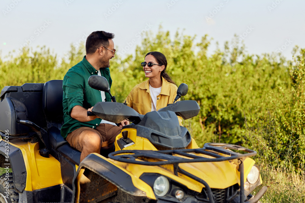 A smiling woman stands outdoors beside her boyfriend on a rental quad bike.