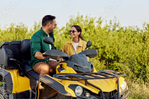 A smiling woman stands outdoors beside her boyfriend on a rental quad bike.