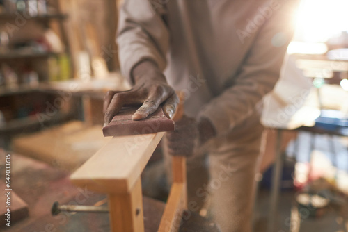 Close up of black craftsman carefully sanding wooden furniture in rustic carpentry workshop, copy space