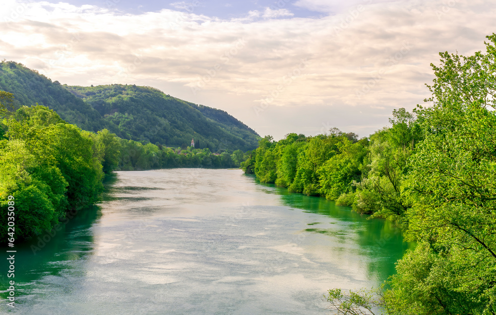 beautiful landscape of spring or summer sunset river with blue water and green hills on sides and mountains with amazing cloude sky on background