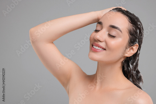 Beautiful happy woman washing hair on grey background. Space for text