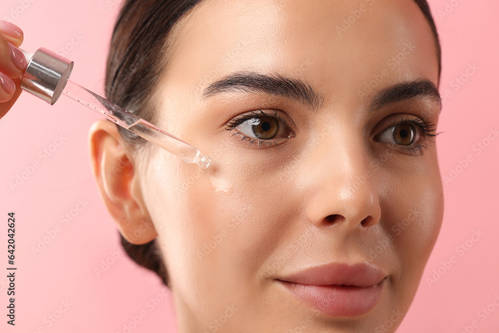 Beautiful young woman applying serum onto her face on pink background, closeup Beautiful young woman applying serum onto her face on pink background, closeup