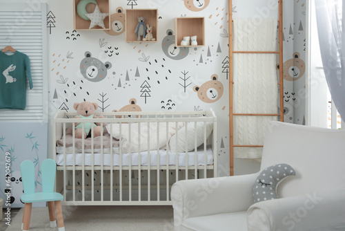 Stylish baby room interior with crib, armchair and cute wallpapers