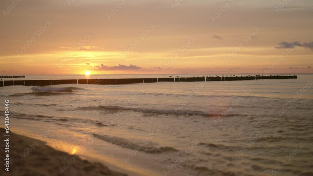Lovely beach at the coastline. Waves crashing at breakwater with beautiful setting sun at dusk Lovely beach at the coastline. Waves crashing at breakwater with beautiful setting sun at dusk