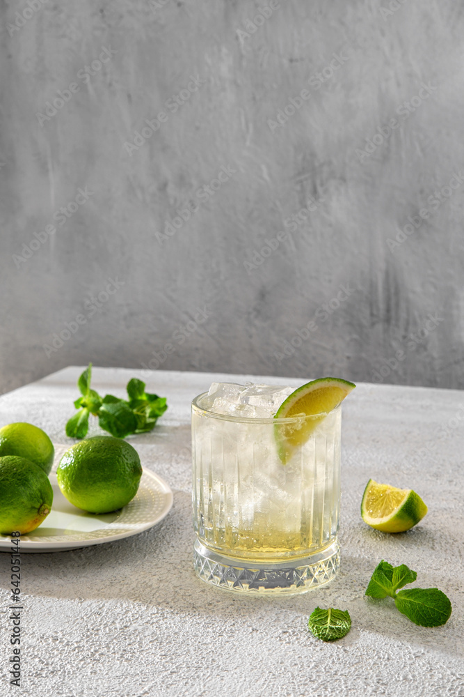 Fototapeta premium Brazilian traditional caipirinha cocktail made with lime, cachaça and sugar. Fresh summer caipirinha cocktail with green fruit lime on table