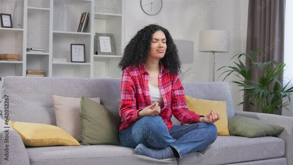 Angle view of healthy concentrated yoga practitioner keeping eyes closed and meditating in stylish apartment. African american woman sitting in lotus position with crossed legs and relaxing body. Angle view of healthy concentrated yoga practitioner keeping eyes closed and meditating in stylish apartment. African american woman sitting in lotus position with crossed legs and relaxing body.