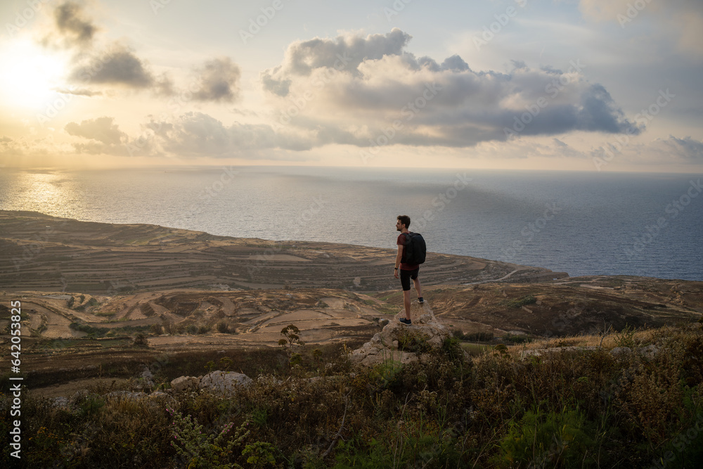 Photo of a man enjoying the breathtaking view of the ocean at sunset from the top of a hill