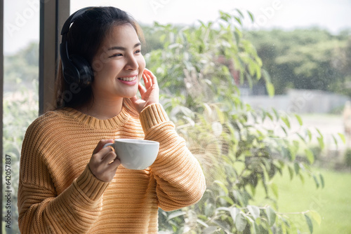 Portrait of beautiful young woman with a cup of coffee and wearing headphones standing relaxed and happy.