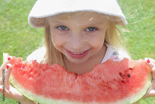 Happy little girl with big watermelon slice. Cild eating fruit. Outdoor close up portrait. photo