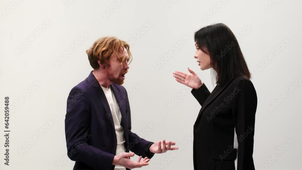 Angry young couple quarreling, actively gesticulating, talking and yelling at each other on a white isolated background. Unhappy man and woman arguing, studio portrait. Angry young couple quarreling, actively gesticulating, talking and yelling at each other on a white isolated background. Unhappy man and woman arguing, studio portrait.