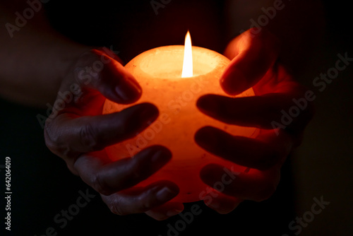 Female hands hold a round white candle with a burning flame