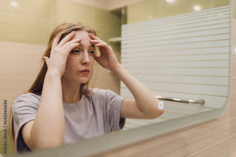 Young woman looks at herself in the mirror standing in the bathroom. Young woman looks at herself in the mirror standing in the bathroom.