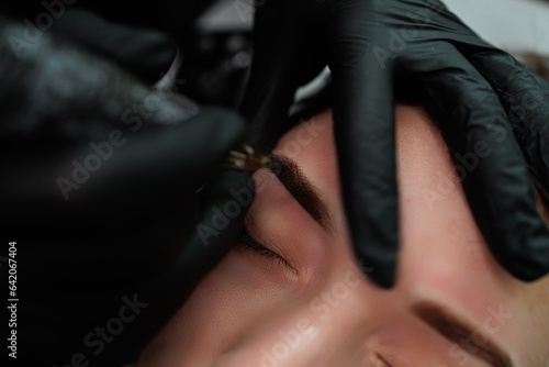 Macro photo of the process of applying permanent makeup on the eyebrow. Eyebrow permanent makeup cosmetic procedure.