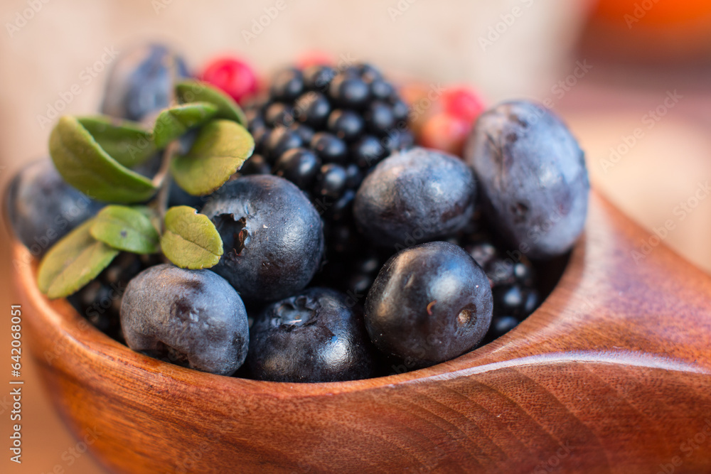 Blackberries, cranberries and blueberries in a wooden cup on the table. Village concept Blackberries, cranberries and blueberries in a wooden cup on the table. Village concept