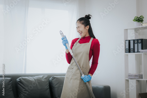 Happy Asian woman cleaning the house Hold the mop like you use a microphone. Housewives enjoy creative chores and house cleaning.