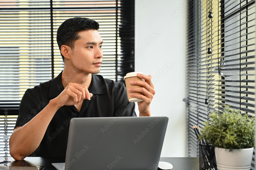 Young Asian adult businessman working at office desk while looking out of the window Young Asian adult businessman working at office desk while looking out of the window