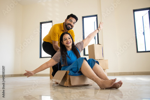 Happy young indian couple having fun in new home. Playing with boxes, Real estate, residential mortgage, moving into dream house concept. photo