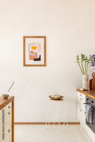 Minimalist composition of kitchen interior with mock up poster frame, white kitchen furniture, wooden kitchen island, induction hob, stool with bowl, pear and personal accessories. Home decor Template