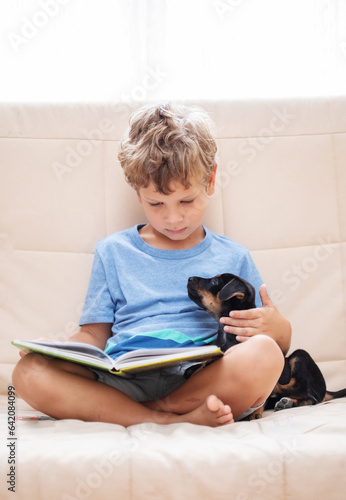 A boy with a little dog is reading a book