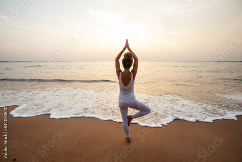 Woman practicing yoga by the ocean at dawn