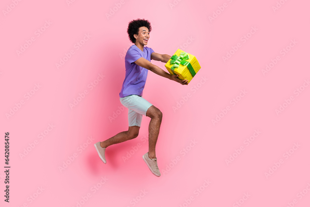 Full length photo of crazy ecstatic man dressed blue t-shirt run look empty space hold present box isolated on pink color background Full length photo of crazy ecstatic man dressed blue t-shirt run look empty space hold present box isolated on pink color background