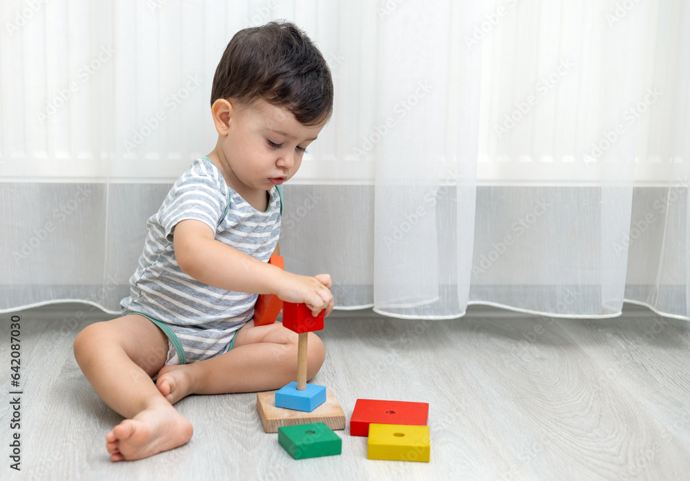 baby boy kid playing with construction wooden or plastic blocks, toy pyramid on floor inside room in front of mirror.adorable child baby boy kid playing with construction wooden or plastic blocks, toy pyramid on floor inside room in front of mirror.adorable child