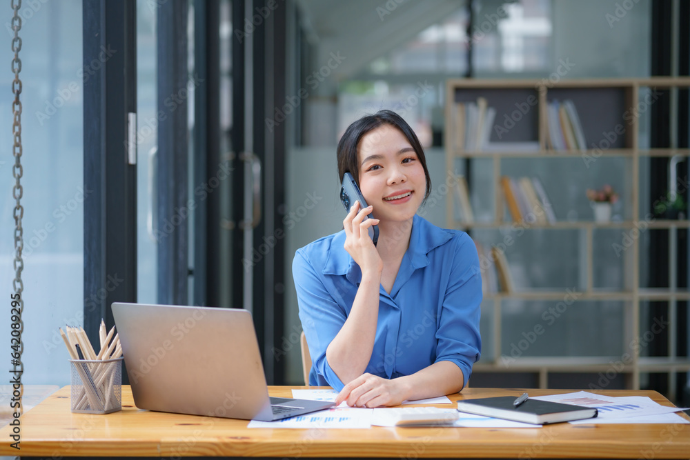 Beautiful businesswoman using a smartphone and working with a laptop while sitting at an office desk, working from home concept. Beautiful businesswoman using a smartphone and working with a laptop while sitting at an office desk, working from home concept.