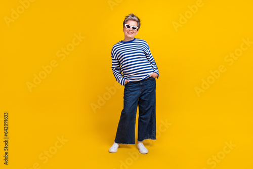 Full length photo of gorgeous lovely lady stylish pensioner nice outfit hands in pockets good mood isolated on yellow color background