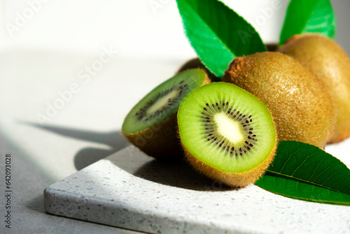 Ripe kiwi fruits in sunlight. Heap of whole kiwi fruits with green leaves and fresh cut kiwi on table. Healthy organic fruits full of vitamins and antioxidants.
