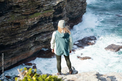 Woman standing on a rock onto of a cliff looking out at the view of the ocean  photo