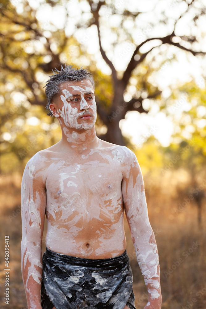 Young aboriginal man with neutral expression standing on country with ochre body paint Young aboriginal man with neutral expression standing on country with ochre body paint