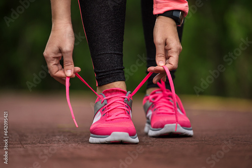 Fitness woman tying running shoe laces, ready for jogging in summer park. Healthy lifestyle