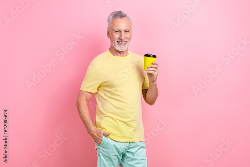 Portrait of positive cheerful person wear stylish t-shirt hold takeway cup of latte arm in pocket isolated on pink color background photo