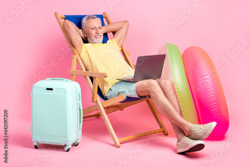 Full body photo nap sleepy senior man hands head lying sunbed comfort watching netbook business course isolated on pink color background © deagreez