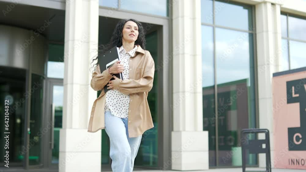 Young female employee is running to a business meeting, going outside from the front door of an office building. Businesswoman with a folder is going to a conference. Brunette woman is late for work Young female employee is running to a business meeting, going outside from the front door of an office building. Businesswoman with a folder is going to a conference. Brunette woman is late for work