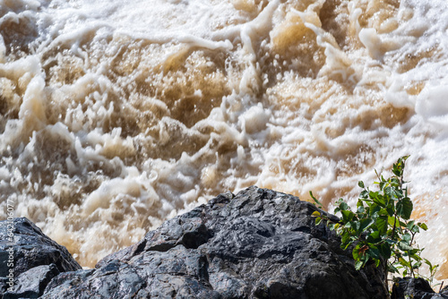 muddy turbulent stream under a rock during high water photo