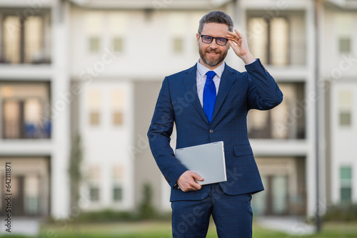 Business man hold laptop outdoor near home. Hispanic man with laptop outdoor. Businessman hold laptop computer front of house background. Entrepreneur with a laptops, business man using laptop. photo