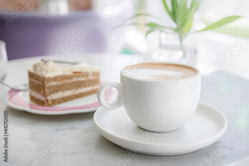 A delicious snack and a mug of hot cappuccino coffee. A piece of cake on the table is a great opportunity to take a break in the afternoon for a pleasant snack.