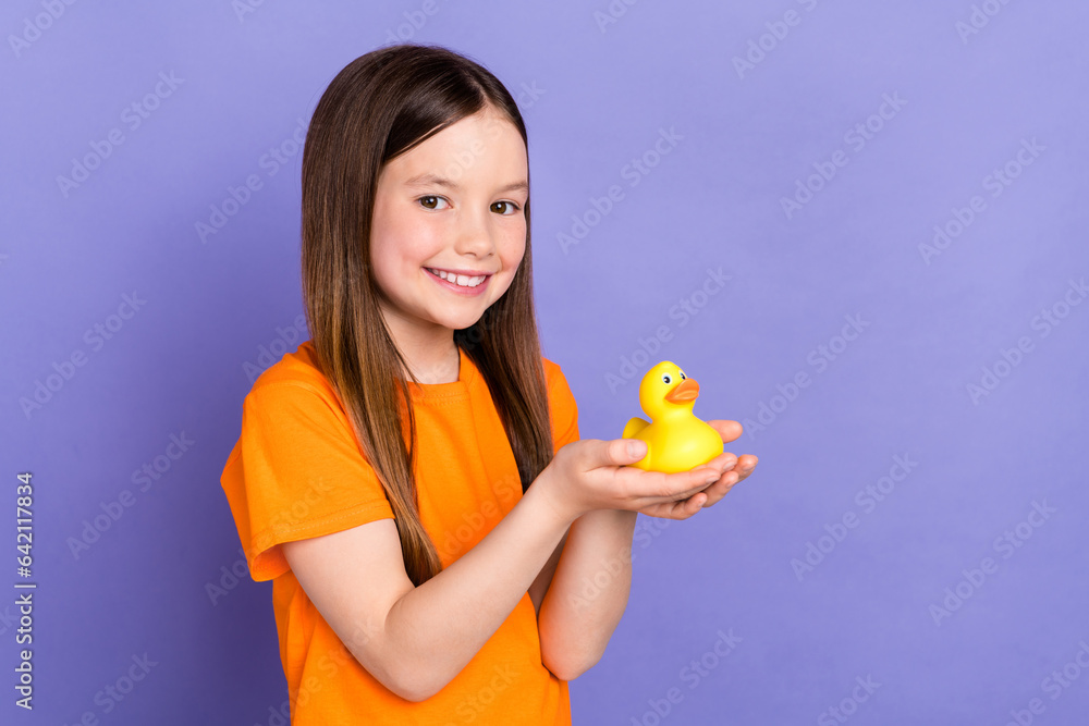 Portrait of satisfied lovely cute schoolgirl with long hairdo wear stylish t-shirt hold duck toy isolated on violet color background Portrait of satisfied lovely cute schoolgirl with long hairdo wear stylish t-shirt hold duck toy isolated on violet color background