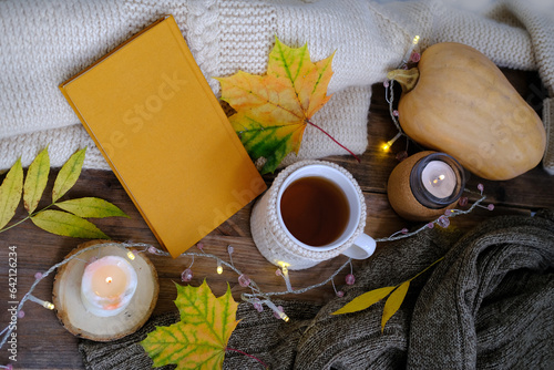 autumn flatlay in style Scandinavian hugg with tea in mugwarm woolen clothes, yellow leaves, book on wooden table, garlands, candle is burning, concept of tea party, good weather, cozy autumn photo