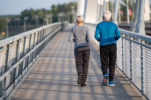 Cheerful active senior couple jogging together outdoors on the bridge. Healthy activities for elderly people.