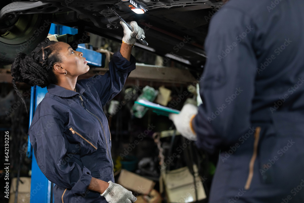 African female mechanic checking and fixing underneath car in automobile repair shop