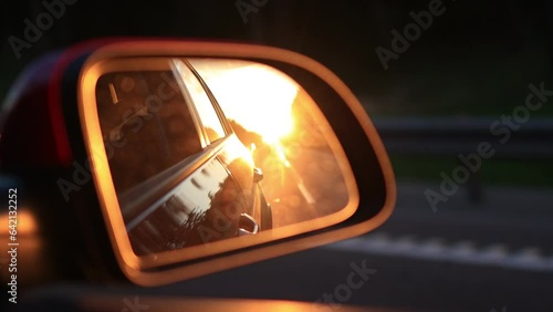 The sun is reflected in the mirror, evening road. View in the rear view side mirror of a auto, driving a red car along the track photo